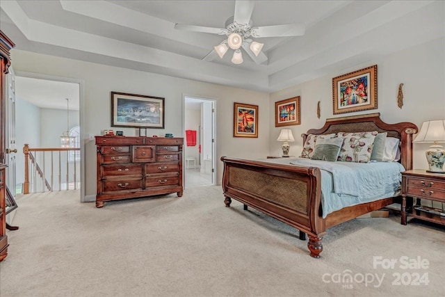 bedroom with ceiling fan with notable chandelier, light colored carpet, a raised ceiling, and ensuite bathroom