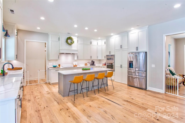 kitchen featuring a breakfast bar area, stainless steel appliances, white cabinets, and light wood-type flooring