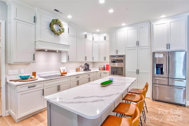 kitchen featuring a breakfast bar, a center island, appliances with stainless steel finishes, light hardwood / wood-style flooring, and white cabinets