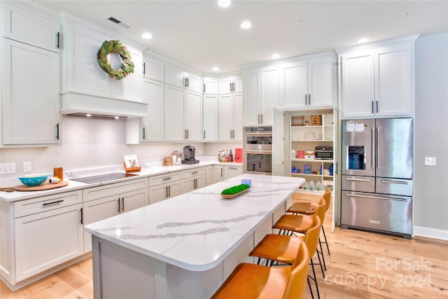 kitchen featuring appliances with stainless steel finishes, light hardwood / wood-style flooring, a kitchen bar, and white cabinets