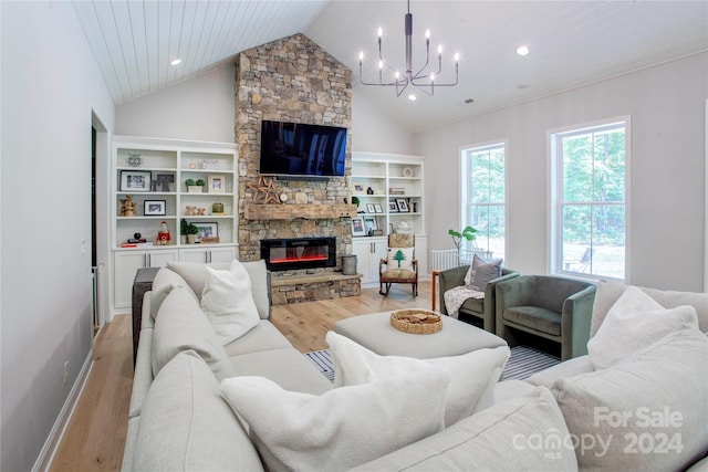 living room with light hardwood / wood-style floors, a stone fireplace, built in shelves, and a chandelier