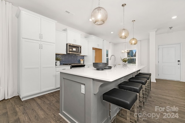 kitchen with pendant lighting, stainless steel appliances, white cabinetry, and an island with sink