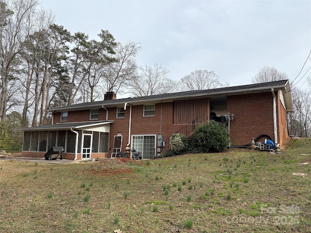 rear view of house featuring a sunroom, brick siding, a lawn, and a chimney