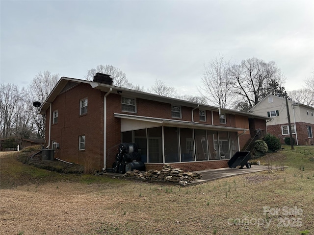 rear view of house featuring a yard, brick siding, a chimney, and a sunroom