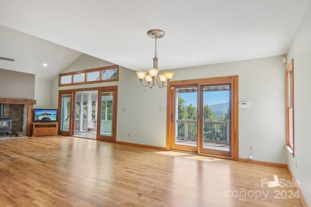 unfurnished living room with a chandelier, a wood stove, vaulted ceiling, light hardwood / wood-style floors, and a fireplace