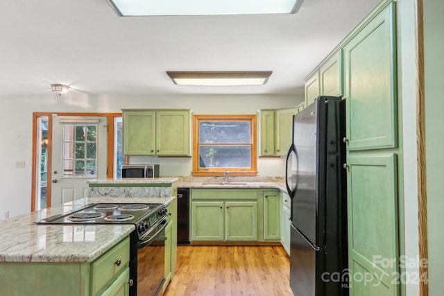 kitchen featuring sink, green cabinets, light stone countertops, light hardwood / wood-style floors, and black appliances