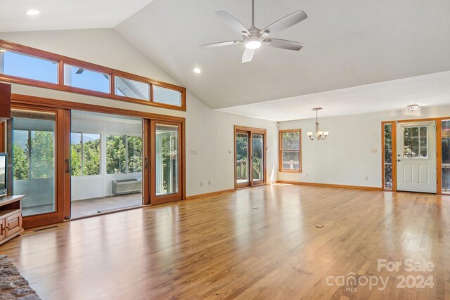 unfurnished living room with high vaulted ceiling, light hardwood / wood-style floors, ceiling fan with notable chandelier, and an AC wall unit