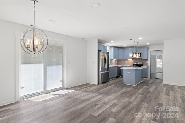 kitchen featuring wood finished floors, decorative backsplash, an inviting chandelier, stainless steel appliances, and light countertops