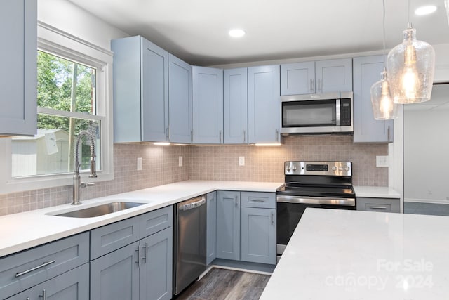 kitchen featuring stainless steel appliances, light countertops, a sink, hanging light fixtures, and dark wood-style flooring