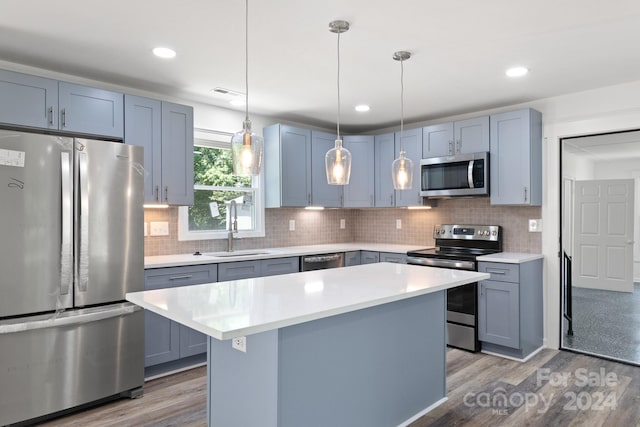 kitchen featuring appliances with stainless steel finishes, decorative light fixtures, backsplash, sink, and hardwood / wood-style flooring