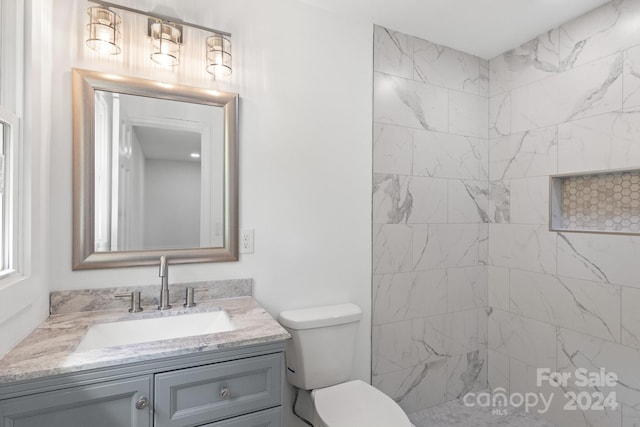 bathroom with a tile shower, toilet, and vanity