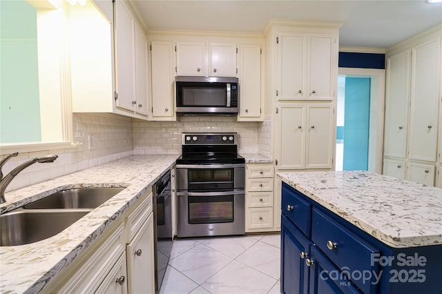 kitchen featuring blue cabinetry, sink, tasteful backsplash, light stone counters, and appliances with stainless steel finishes