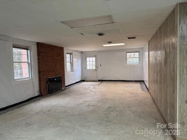 unfurnished living room with a healthy amount of sunlight, wooden walls, and a brick fireplace