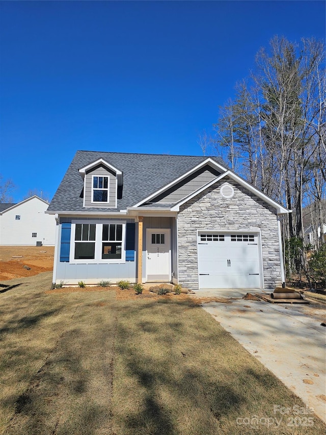 view of front of house with a shingled roof, an attached garage, stone siding, driveway, and a front lawn