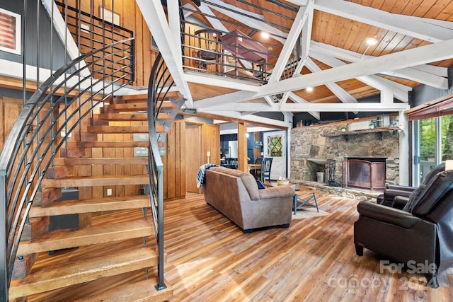 living area with wood ceiling, a stone fireplace, wood finished floors, beamed ceiling, and stairs