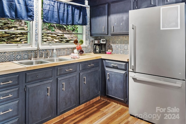 kitchen with butcher block countertops, freestanding refrigerator, a sink, light wood-type flooring, and backsplash