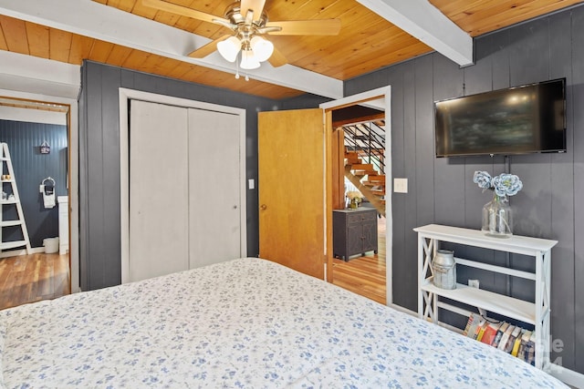 bedroom featuring wood walls, beam ceiling, ceiling fan, and wood-type flooring