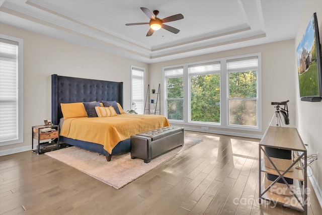 bedroom featuring wood-type flooring, a tray ceiling, ceiling fan, and ornamental molding