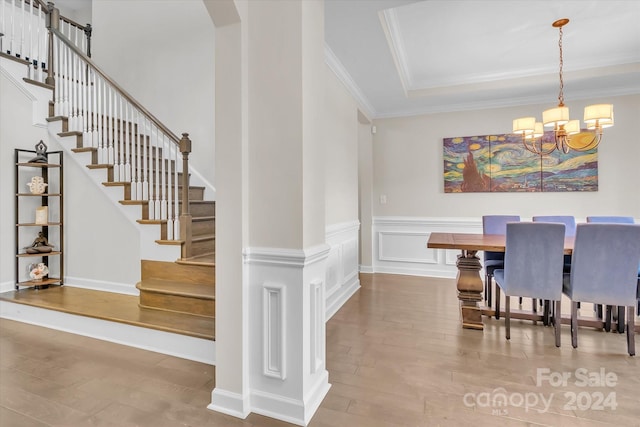 dining space with wood-type flooring, a tray ceiling, ornamental molding, and a notable chandelier