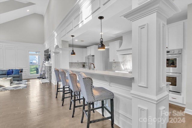 kitchen featuring hanging light fixtures, premium range hood, appliances with stainless steel finishes, white cabinets, and light wood-type flooring