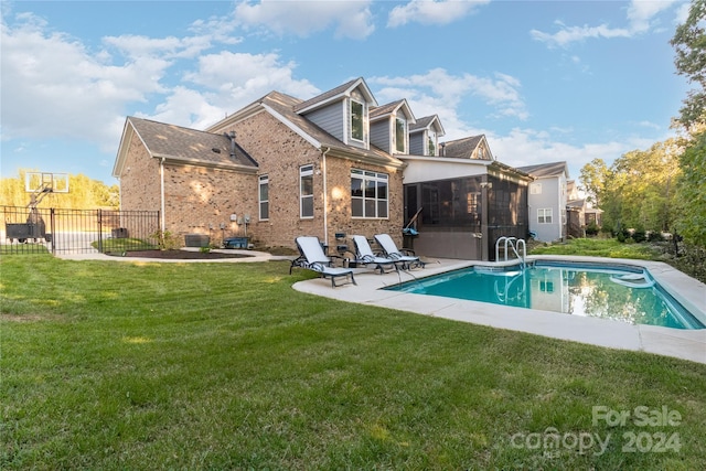 rear view of house with a sunroom, a patio area, a fenced in pool, and a lawn