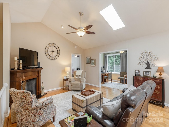 living room featuring high vaulted ceiling, ceiling fan, a skylight, and light wood-type flooring