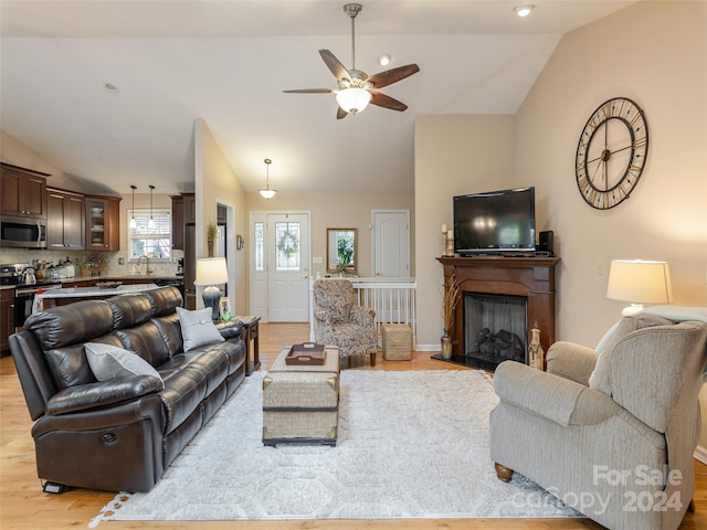 living room with light wood-type flooring, vaulted ceiling, sink, and ceiling fan