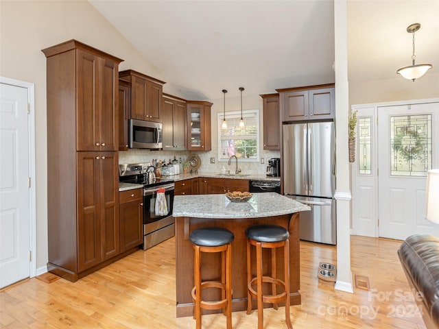 kitchen with appliances with stainless steel finishes, decorative light fixtures, backsplash, light wood-type flooring, and lofted ceiling