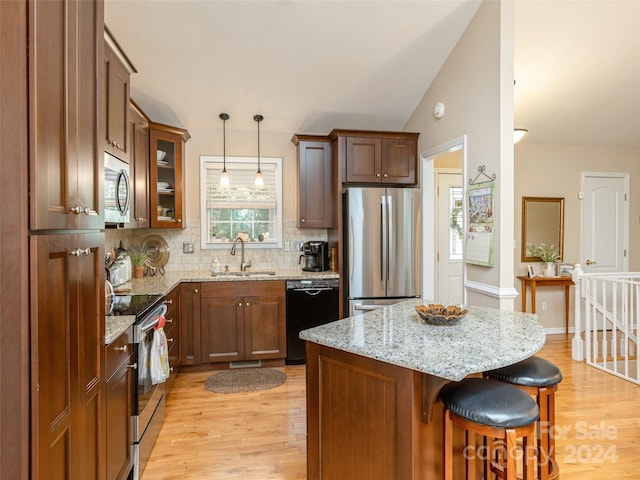 kitchen with appliances with stainless steel finishes, light hardwood / wood-style flooring, pendant lighting, and sink