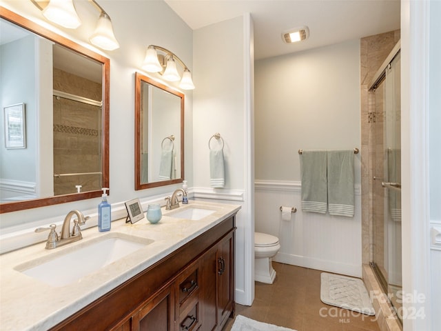 bathroom featuring tile patterned flooring, double sink vanity, an enclosed shower, and toilet