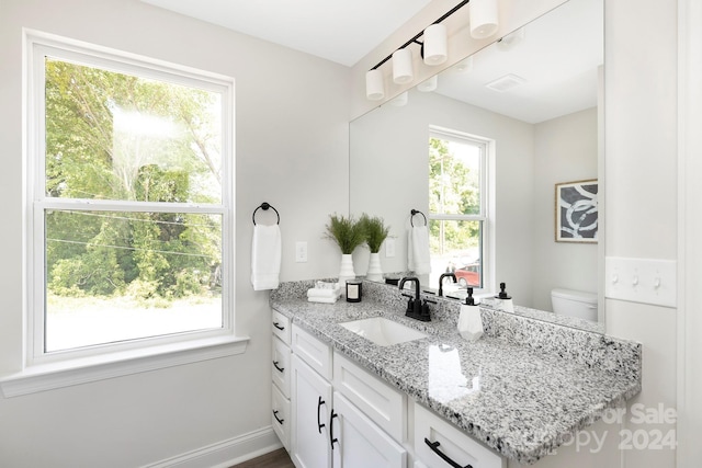 bathroom with toilet, plenty of natural light, vanity, and baseboards