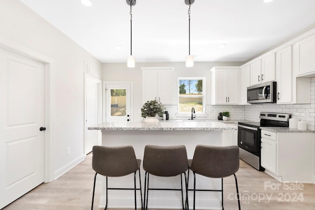 kitchen with a breakfast bar, white cabinets, stainless steel appliances, and decorative backsplash