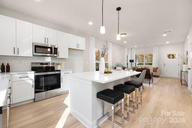 kitchen with white cabinetry, hanging light fixtures, a kitchen island, and stainless steel appliances