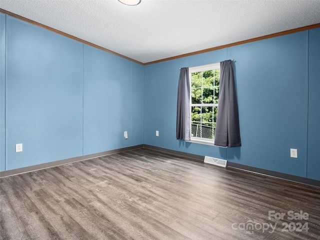 empty room featuring wood finished floors, crown molding, visible vents, and a textured ceiling