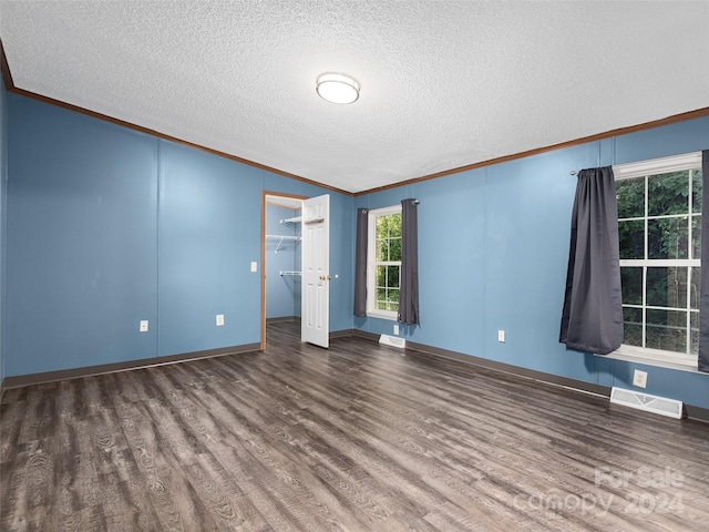 empty room with ornamental molding, dark wood finished floors, a textured ceiling, and visible vents