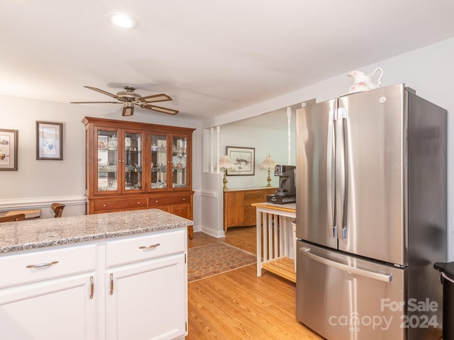 kitchen featuring light stone countertops, ceiling fan, light hardwood / wood-style floors, white cabinetry, and stainless steel refrigerator