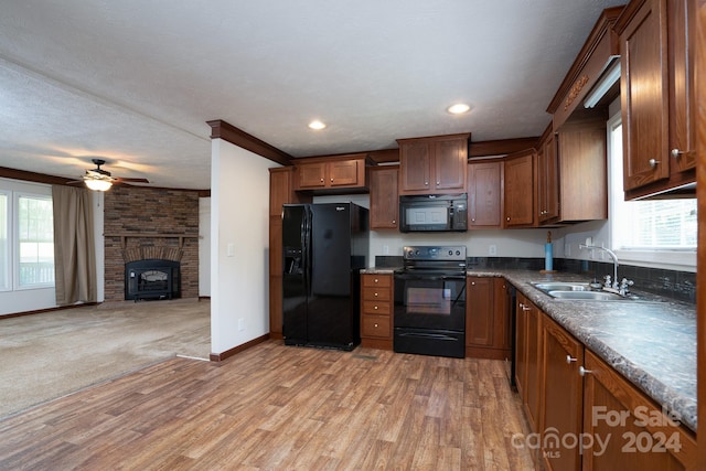 kitchen featuring sink, black appliances, ceiling fan, light carpet, and a brick fireplace