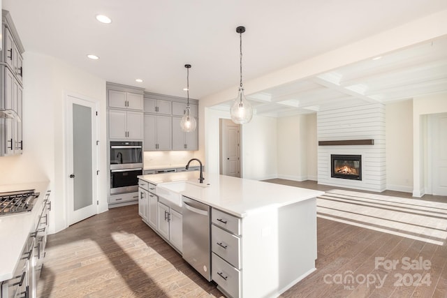 kitchen with hardwood / wood-style flooring, a kitchen island with sink, sink, hanging light fixtures, and appliances with stainless steel finishes