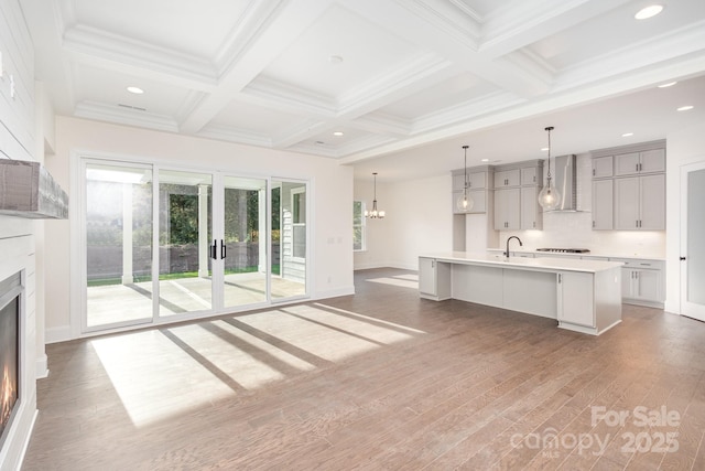 unfurnished living room featuring coffered ceiling, hardwood / wood-style flooring, a chandelier, and beamed ceiling