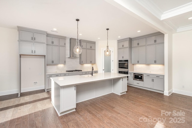 kitchen with sink, gray cabinetry, a kitchen island with sink, gas stovetop, and wall chimney range hood