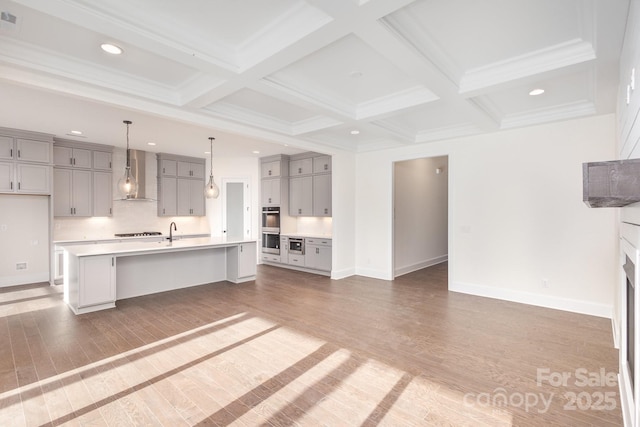 kitchen featuring decorative light fixtures, coffered ceiling, wall chimney exhaust hood, dark wood-type flooring, and a spacious island