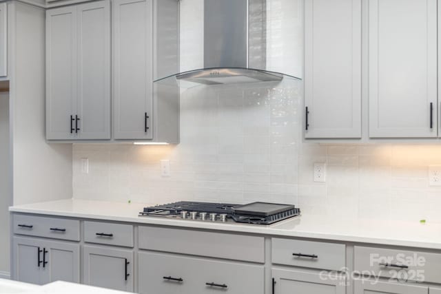 kitchen featuring tasteful backsplash, wall chimney exhaust hood, gray cabinets, and stainless steel gas cooktop