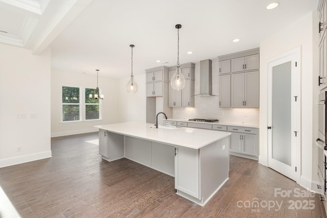 kitchen featuring gas cooktop, wood finished floors, a sink, decorative backsplash, and wall chimney exhaust hood