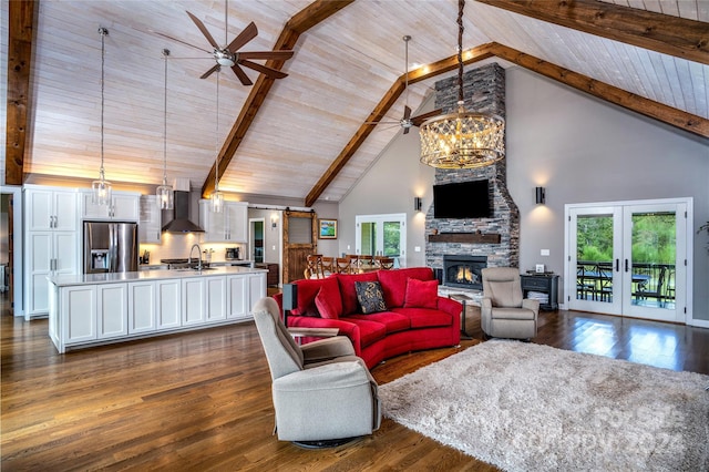 living room with beamed ceiling, ceiling fan with notable chandelier, a stone fireplace, dark wood-type flooring, and high vaulted ceiling