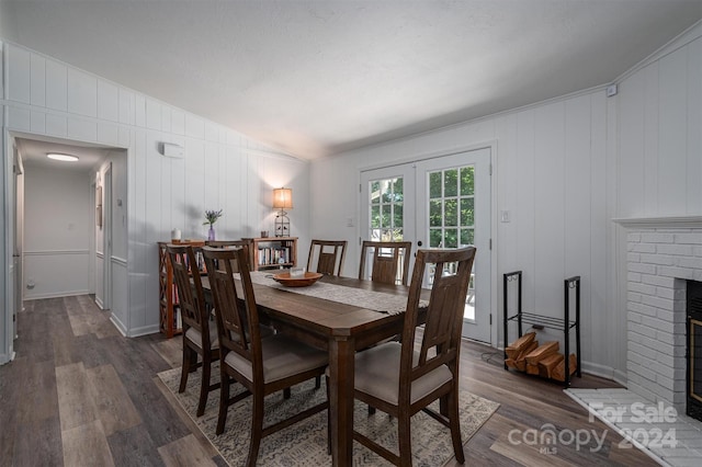 dining space featuring wood walls, french doors, vaulted ceiling, a brick fireplace, and dark hardwood / wood-style floors