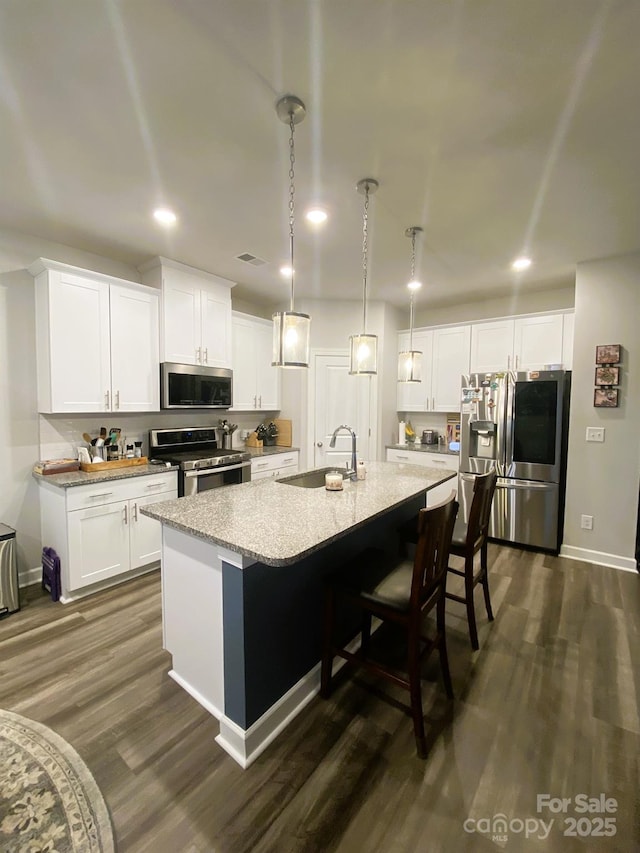 kitchen featuring sink, decorative light fixtures, appliances with stainless steel finishes, a kitchen island with sink, and white cabinets