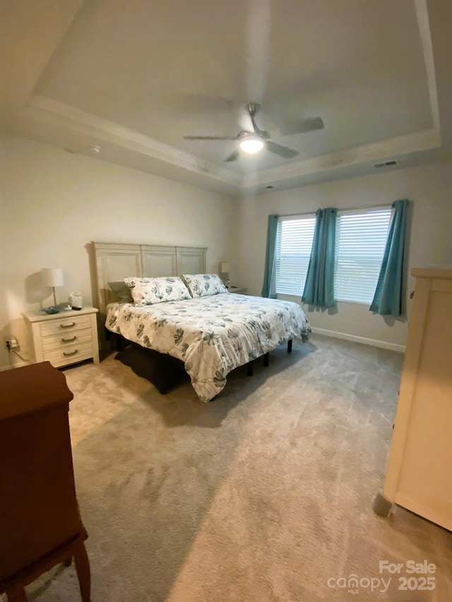 bedroom with a raised ceiling, light colored carpet, and ceiling fan