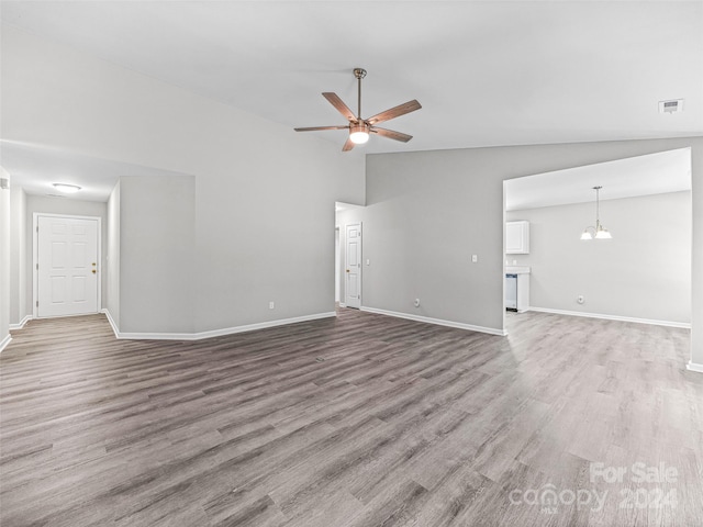 empty room featuring hardwood / wood-style floors, ceiling fan with notable chandelier, and lofted ceiling