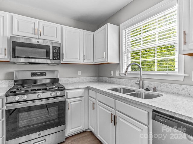 kitchen featuring light hardwood / wood-style flooring, white cabinetry, appliances with stainless steel finishes, light stone counters, and sink