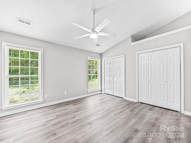 unfurnished bedroom featuring two closets, light hardwood / wood-style flooring, multiple windows, and lofted ceiling